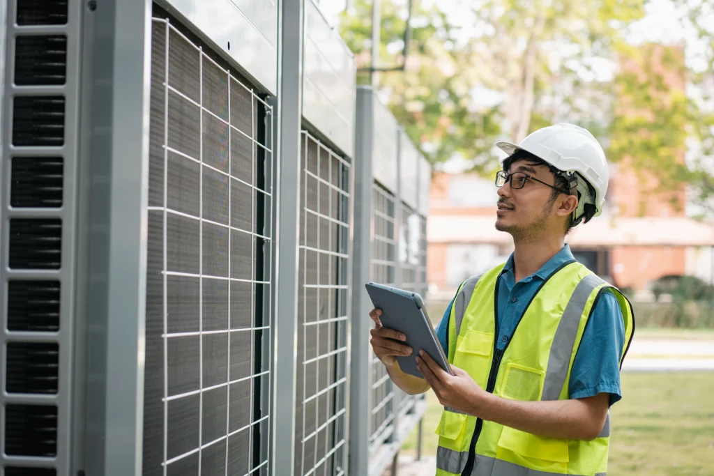 Industrial air conditioning repair engineer inspecting large outdoor AC units with a tablet
